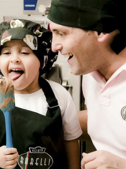 Pai e filha sorrindo na produção da Gelato Borelli, provando o creme na espátula