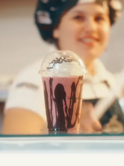 Atendente entregando um milkshake com calda de chocolate no balcão