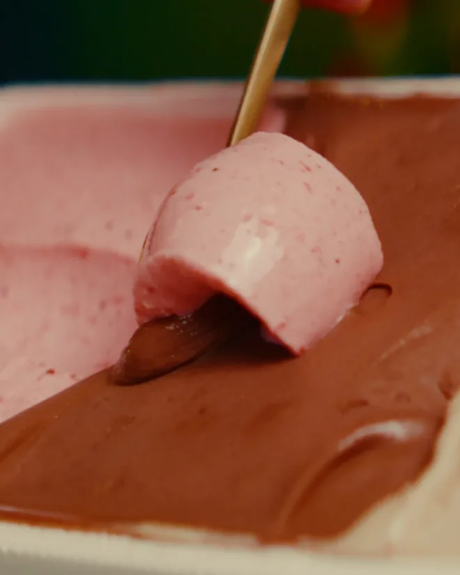 Espátula recolhendo gelato de morango sobre a cuba de chocolate, na produção diária